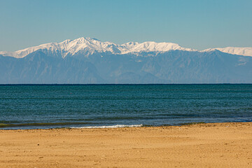 A deserted sandy beach in Side during low season, with turquoise Mediterranean waters meeting snow-capped Taurus Mountains on the horizon. Winter serenity and minimalist beauty. Antalya, Turkey.

