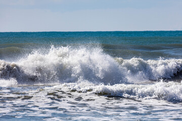A powerful storm wave explodes on the shallow coastal shelf, creating a spectacular swirl of white foam and spray that glitters in the winter sunlight. Minimalist marine power. Antalya, Turkey.


