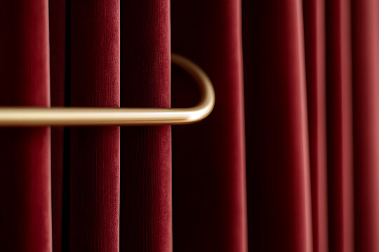 Detailed view of rich, red velvet curtains hanging from a sleek, gold-colored rod. The soft folds and textures create a sense of luxury and privacy. Dramatic stage setting evokes anticipation.