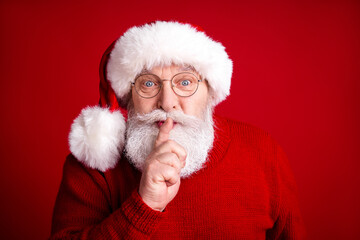 Naklejka premium Santa with a fluffy white beard wearing a red sweater and hat quietly shushing you for a festive Christmas stock photo