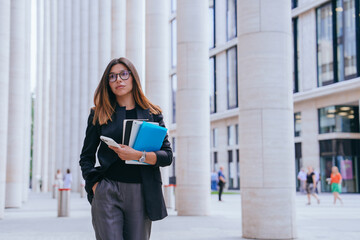 With a phone and files in hand, a woman strides purposefully among monumental columns, embodying...
