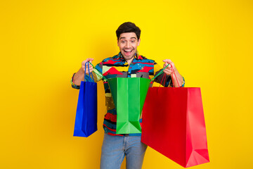 Young man with colorful shirt and shopping bags smiles against bright yellow background