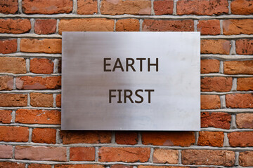 Fototapeta premium A striking metal sign displays the words EARTH FIRST against a textured brick wall, conveying a powerful message about environmental responsibility and conservation efforts