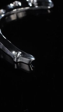 Titanium dental framework shows curved arch and joint elements against deep black. Shaped metal follows tooth line while precise edges support implant connection and strong fixation vertical video