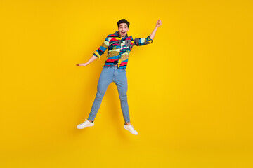 Young man jumping in a colorful print shirt against a bright yellow background for a fun casual fashion lifestyle image