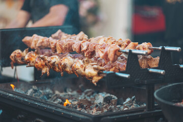 Sizzling skewers of marinated meat grilling over open flames in a vibrant outdoor market during a summer festival