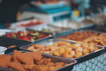Exquisite array of traditional snacks displayed on metal trays at a bustling outdoor market in the early afternoon sun