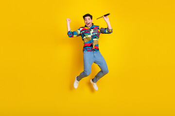 Energetic young man leaps in a colorful print shirt with microphone on a bright yellow background stock photo