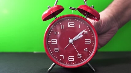 A person gently sets a red alarm clock while its hands move from 3AM to 2AM in Daylight saving time end