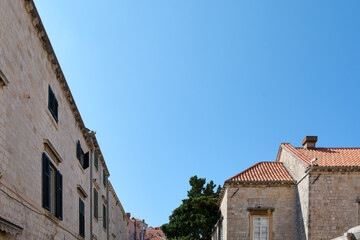 Low-angle view of stone buildings with terracotta roofs and green shutters in a European travel destination. The bright blue sky provides ample copy space.