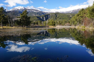 mountain landscape with small lake and mirror reflection of the peaks in southern alps, france