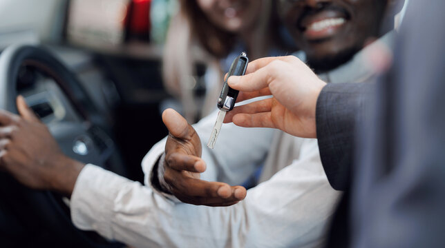 Happy family couple choosing and buying car at vehicle showroom. Salesman consultation and hands over key to client