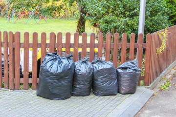 Black garbage bags placed beside brown wooden fence in residential Warsaw neighborhood during autumn season. High quality photograph.