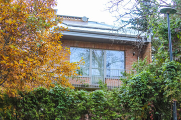 Residential house with peaked roof surrounded by autumn trees in quiet Warsaw Poland suburban neighborhood. High quality photograph.