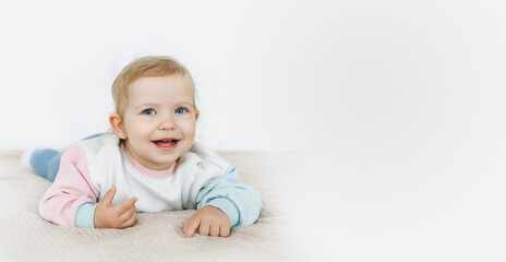 Fototapeta premium Smiling baby 6-12 months old lying on his stomach on a white bed.