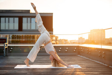 Woman practicing yoga on rooftop at sunset