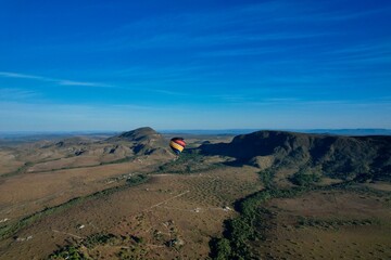 Hot air balloon flying over green fields and mountains under clear blue sky in Brazil