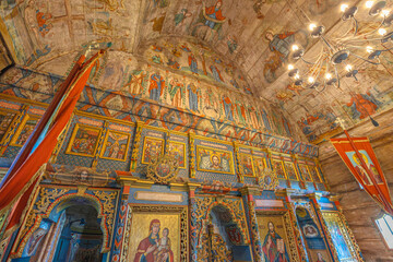 Maramures, Romania - Aug 13, 2025: Ornate 18th-century wooden Church of the Archangels Michael and Gabriel in Plopis, Maramures, Romania, with painted icons, colorful textile benches, carved woodwork