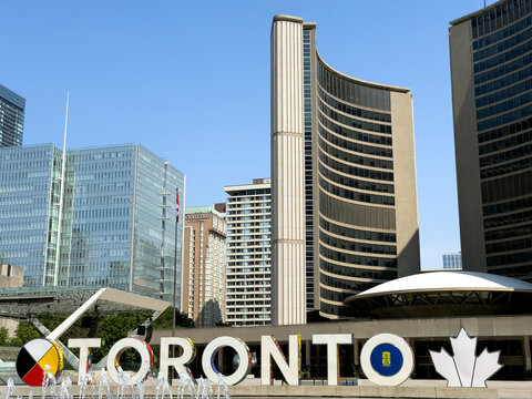 Downtown Toronto skyline with curved towers of City Hall, large TORONTO sign and and surrounding skyscrapers in Nathan Phillips Square - Toronto, Canada - June 22, 2025