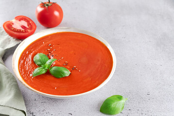 Fresh tomato cream soup with basil leaves, cherry tomatoes on gray background. Vegetarian food.