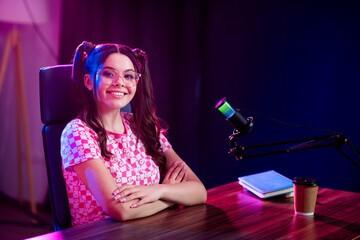 Popular female content creator sitting in a modern home studio with bright neon lights and professional recording equipment.