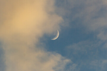 Crescent moon in the blue sky with white clouds