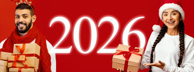 Two smiling individuals dressed in festive attire are holding wrapped gifts against a bright red background. The year 2026 is prominently displayed, signaling celebration.