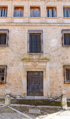 Fototapeta premium Close-up of a traditional stone building in Chinchón featuring worn windows with rusted iron grates, a weathered wooden door, and old posts in the foreground.