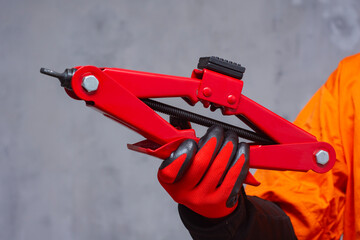 Close-up of a mechanic wearing black protective gloves holding an red car jack tool. Concept of automotive repair, maintenance, and safety equipment.
