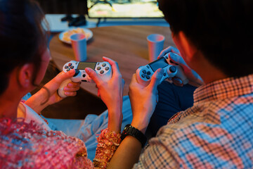 Cropped of hands couple with joysticks sitting sofa playing video game together at back side view...