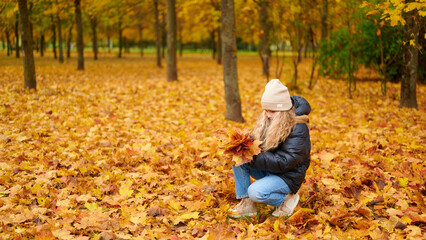 woman in park holding autumn leaves amidst colorful foliage, wearing warm clothing and beanie. captures essence of fall, outdoor relaxation, tranquility, and nature's beauty.