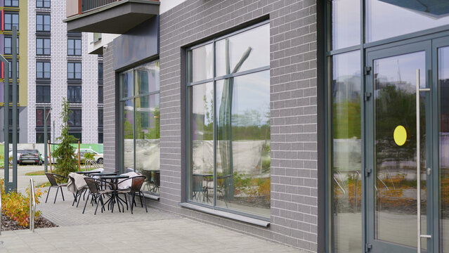 modern outdoor cafe seating area with empty tables and chairs on urban sidewalk. contemporary building design features large glass windows. inviting space for relaxation and socializing - Powered by Adobe