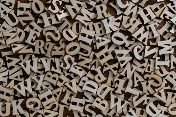 Pile of wooden letters of the English alphabet, laid out in a chaotic order on a table, closeup, top view. Background of many wooden letters