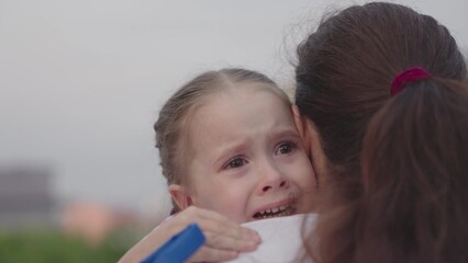 a small child sheds tears on the shoulder of an embracing mother, crying of an upset kid, childhood emotions of a capricious baby, a problem for an unhappy girl, experiencing pain of strong feelings.