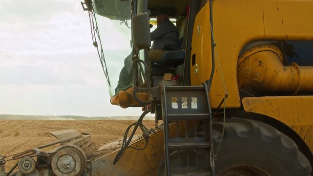 Detail shot of industrial combine harvester in field with bearded man inspecting vehicle and cleaning off parts, copy space