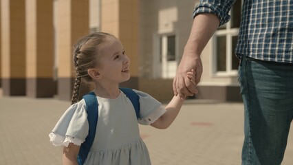 Dad leads the child by hand to school, close-up, a little schoolgirl with backpack, a happy family, a kid's childhood dream, an active student girl, good modern education, love and receive knowledge.