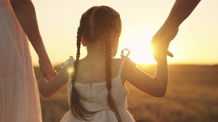 cheerful girl holding her parents' hands at sunset in sky, happy family, childhood dream, child with mom and dad in sun, little kid walks with father mother, family day, travel with baby hand in hand.