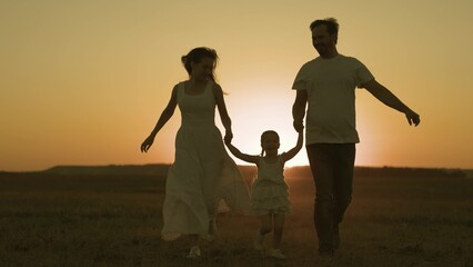 Happy father and mother run across field with small child sunset in sky, silhouette cheerful family, childhood dream of parents, play together, give attention to children, love of mom and dad for kid.