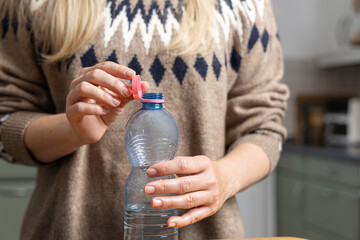 Woman is preparing to recycle plastic bottle by removing cap, demonstrating responsible packaging disposal and environmental awareness in kitchen setting