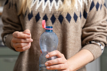 Bottle with stationary plastic cap in woman hand. The new design means the cap remains attached to the bottle after opening, making the entire package easier to collect and recycle