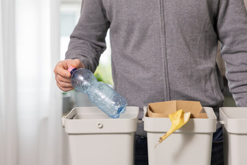 Individual recycling plastic bottle into bin while sorting waste at home, promoting sustainability and eco-friendly practices in daily life