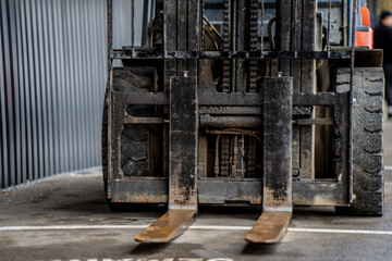 Front view of forklift with visible metal lifting forks and large rubber tires showing industrial machinery detail, hydraulic lifting system and durable engineering equipment
