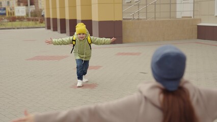 little girl schoolgirl with backpack runs hug her mother, kid rejoice over lessons, happy family, school bag behind back cheerful laughing child, baby hurries her mother her arms, jogging school yard.