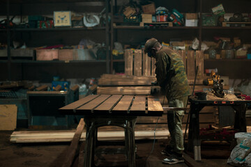 Factory contrasting lighting of a working workshop. Beautiful gloomy photo of a factory worker in a mask and uniform standing at a table operating a grinding machine. High quality photo
