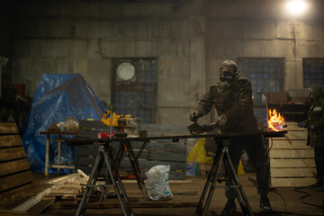 Fototapeta premium Factory contrasting lighting of a working workshop. Beautiful gloomy photo of a factory worker in a mask and uniform standing at a table operating a grinding machine. High quality photo