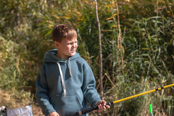 An impatient nine year old boy with a fishing rod in his hands is fishing on a river