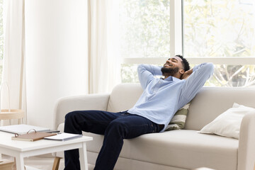 Serene African man relaxing with hands behind head on sofa