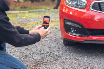 A young man examines and photographs the deformation of the body of his car.