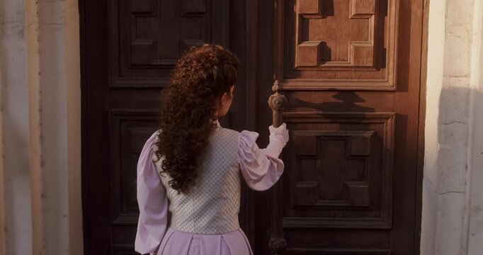 A close up of a woman hand wearing a glove with a decorative ring, knocking on an antique wooden door bathed in warm sunlight, capturing a timeless and cinematic moment.