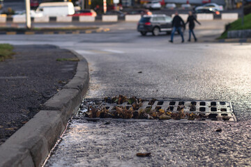 A drain on the road during rainy weather and moving cars in the background